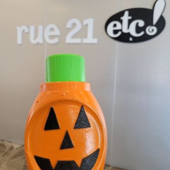 Crystal Mall - A plastic bottle designed as a pumpkin with a jack-o'-lantern face, held in front of a wall with signage reading 'rue 21' and 'etc!'. - Shopping Centers Near Me - Waterford, Connecticut