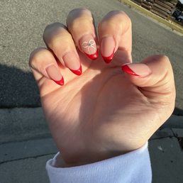 my hand with a red french top and a white bow with a rhinestone on my middle finger