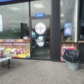 SoBoL - Entrance of the shop on central Park ave. - SoBoL smoothie bowl shop's entrance features a glass door with store hours and branding, surrounded by fruit-themed window graphics. - Juice Bars & Smoothies Near Me - Yonkers, New York