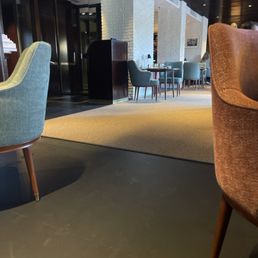 A rug, 2 chairs (more in the background), a door, 3 tables, check-in spot
