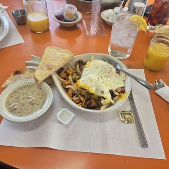 The Farmers Table - I got the 2 egg skillet with onions, bacon, cheese and potatoes. With a side of sausage gravy. - A breakfast meal featuring fried eggs with seasoning, toasted bread, and a bowl of gravy, served on an orange table with drinks and condiments. - Breakfast & Brunch Near Me - Wolverine, Michigan