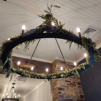 Lindy's Landing - A round chandelier with light bulbs is decorated with greenery and hangs from the ceiling of an indoor dining area. - American Near Me - Wauconda, Illinois