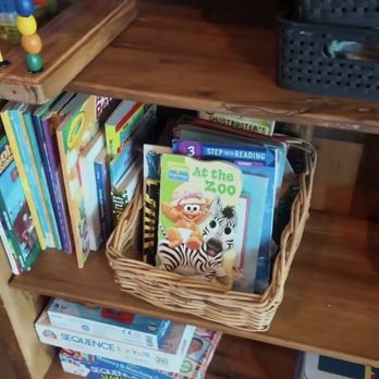 Mac's Local Eats - Bookshelf at front something for kids and they have cards - A wooden bookshelf holds children's books, including 'At the Zoo,' with a basket of books in front and additional books on the shelves. - American Near Me - St Louis, Missouri