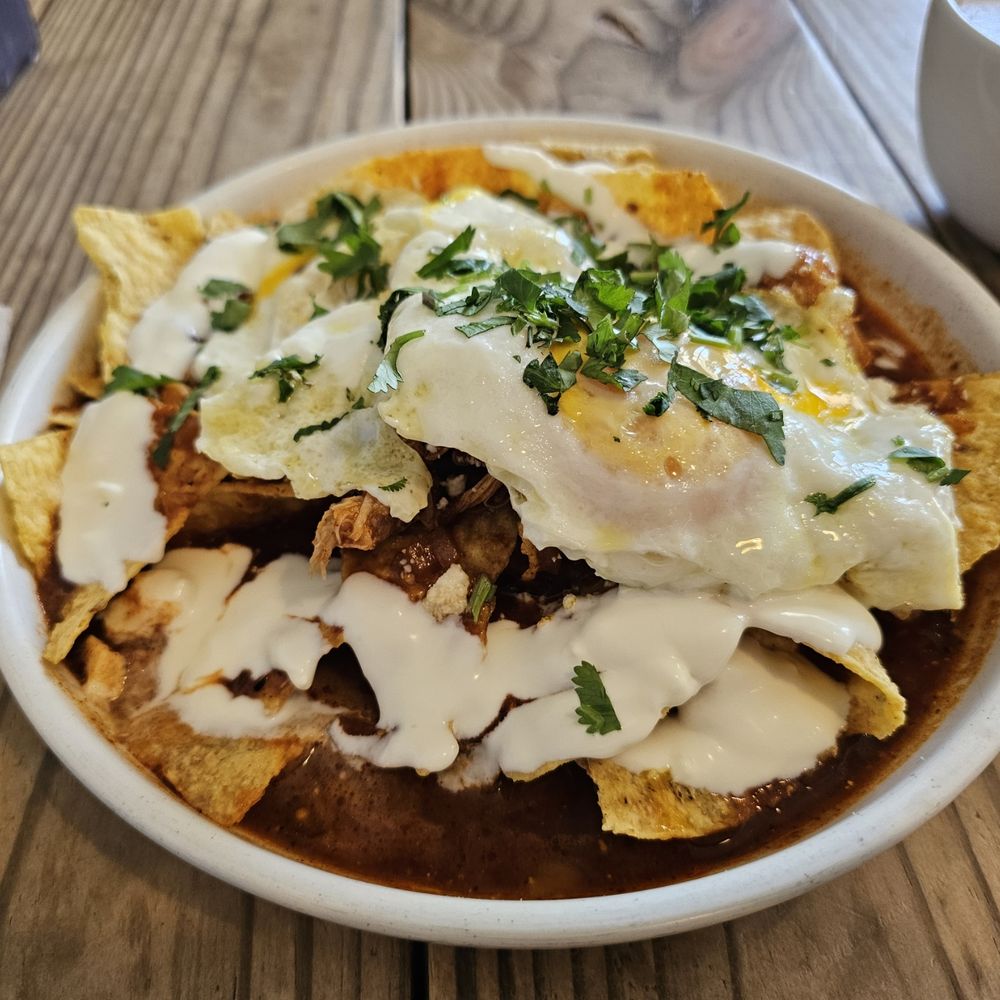 Chilaquiles Rojo with roasted chicken, two over-easy eggs, queso fresco, gluten-free tortilla chips, cilantro, lime, tomato, and spices Chilaquiles Rojo with roasted chicken, two over-easy eggs, queso fresco, gluten-free tortilla chips, cilantro, lime, tomato, and spices