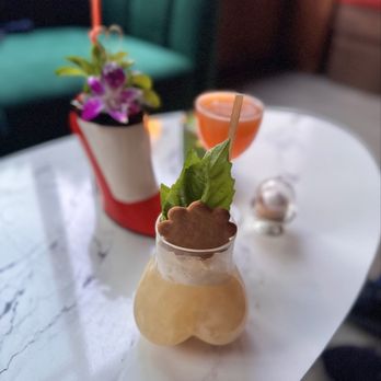 Public Parking - A beverage in a glass with lettuce and a cookie garnish on a white marble table, with a potted plant and another drink in the background. - Bars Near Me - Madison, Wisconsin