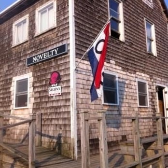The Novelty - a wooden building with a flag on it - American Near Me - Monhegan, Maine The Novelty - a wooden building with a flag on it - American Near Me - Monhegan, Maine