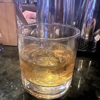 Hooligan's Pub - Sazerac rye on the rocks - A short, clear glass filled with Sazerac rye whiskey on the rocks, placed on a dark bar surface with ice cubes visible. - Pubs Near Me - Arlington, Texas