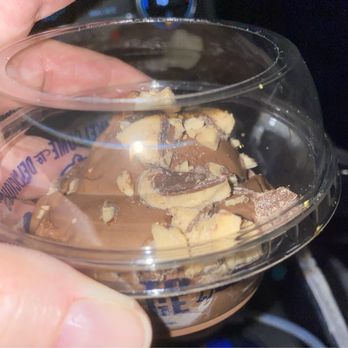 Culver's - Basically half a scoop...pathetic. - A transparent plastic container filled with chocolate ice cream and chocolate chunks is held by a person's hand. The background shows part of a vehicle's dashboard and steering wheel, indicating the photo was taken inside a car. - Fast Food Near Me - Homer Glen, Illinois