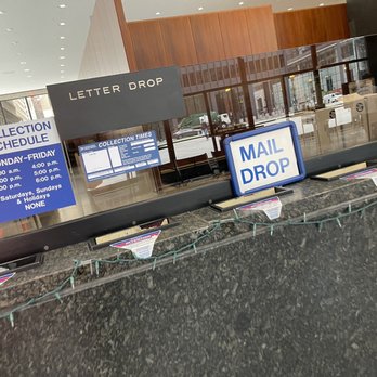 USPS - A USPS mail drop box with signs displaying collection times and schedule, located inside a building with glass windows and reflections. - Post Offices Near Me - Chicago, Illinois