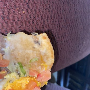 Taco Bell - Taco with mold - A taco with lettuce, tomato, cheese, and a flour tortilla is shown partially eaten on a maroon textured surface. - Tacos Near Me - Lamesa, Texas