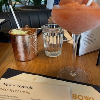 Earls Kitchen + Bar - A restaurant table features a pink frozen cocktail in a tall glass, a copper cup with a straw, and a glass of water, with a menu in the foreground. - Canadian (New) Near Me - Etobicoke, Ontario