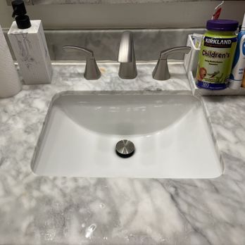 Nelly s Cleaning - My son's Bathroom sink area, very clean and sparkling after cleaning! **Yellow spot in back of sink handle result of granite water damage** - A bathroom vanity with a marble countertop, a white sink, and a silver drain. Toiletries and a tissue box are placed around the sink. - Home Cleaning Near Me