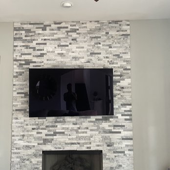 Right Remodeling Services - Tile fireplace - A stone fireplace with a mounted flat-screen TV above it is set against a light-colored wall in a living room. The TV reflects a person taking the photo. - Flooring Near Me