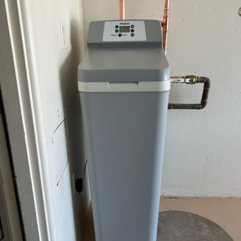 ProSkill Services - A gray Whirlpool water softener is positioned against a wall, connected to copper pipes, in a utility or laundry room. - Plumbing Near Me - Anthem, Arizona