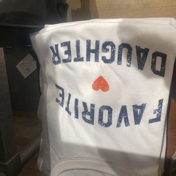 Art Effect - A white sweatshirt with blue text reading 'FAVORITE DAUGHTER' and a red heart in the center, laid on a wooden surface. - Women's Clothing Near Me - Chicago, Illinois