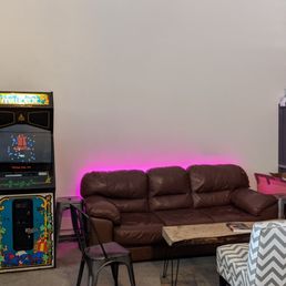 a living room with a couch, chair, and arcade machine a living room with a couch, chair, and arcade machine