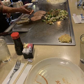 Koze Teppan Grill - A teppanyaki-style restaurant scene with a chef preparing food on a flat-top grill, including rice, vegetables, and meat, with dining utensils and glasses on the table. - Sushi Bars Near Me - El Paso, Texas