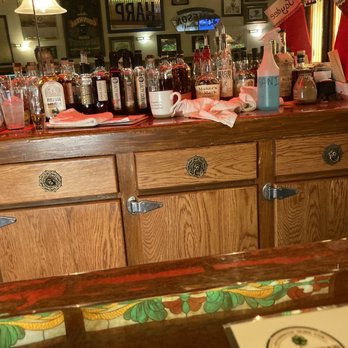 Brazen Head Pub - a bar with a lot of bottles - A bar counter made of wood with a variety of liquor bottles, glasses, and bar tools arranged on top. The background features framed pictures and pub decor, indicating a pub or Irish bar setting. The counter has drawers with decorative handles and a colorful tiled edge at the front. - Pubs Near Me - West Bend, Wisconsin