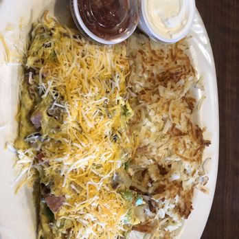 Pegah's - A breakfast plate features an omelette topped with shredded cheese, alongside crispy hash browns, with small containers of syrup and sour cream. - Salad Near Me - Lee's Summit, Missouri