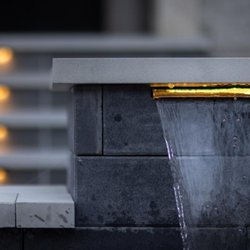 Action Home Services - Modern pool water feature with LED lighting and elegant stone design for a luxury backyard retreat.