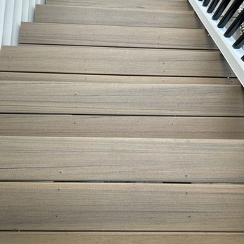 Elite Exteriors - Screws here and there but not everywhere. - A photograph of a wooden deck with horizontal planks, showing a railing with black balusters on the right side. - Roofing Near Me - New Berlin, Wisconsin