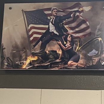 The Angry Elephant - a man holding a gun and a woman kneeling down in front of an american flag - Sports Bars Near Me - Magnolia, Texas The Angry Elephant - a man holding a gun and a woman kneeling down in front of an american flag - Sports Bars Near Me - Magnolia, Texas