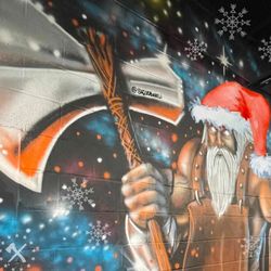 Mural of a warrior in a Santa hat holding an axe, surrounded by snowflakes and stars. Artist: @shobovelli.
