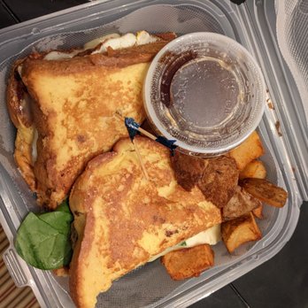 Studio One Cafe - French toast sandwich - A takeout container holds a French toast sandwich with two slices of French toast, potato wedges, a small cup of syrup, and a leaf of lettuce. - Breakfast & Brunch Near Me - Eugene, Oregon