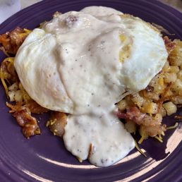 A loaded breakfast dish of eggs, bacon, potatoes and a biscuit with gravy.