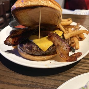 Thirsty Lion - Cheeseburger added bacon - A cheeseburger with bacon, cheddar cheese, and a beef patty is served with French fries and a small container of ketchup on a white plate. - American Near Me - Euless, Texas