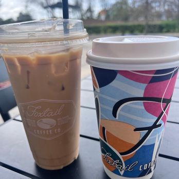 Foxtail Coffee - Riverview - Two iced coffee beverages, one in a clear plastic cup and the other in a colorful paper cup, are placed on a table outdoors at Foxtail Coffee. - Coffee & Tea Near Me - Riverview, Florida