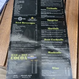 The menu displays a variety of beverage options including iced and hot drinks, cocktails, mocktails, wines, and beers. It features sections for iced beverages like iced coffee and frappes, hot drinks such as hot chocolate and cinnamon bun, and specialty cocktails like Bloody Social and Aperol Spritz. The mocktails include Blue Mule and CosNoPolitan, while wine options list different types with prices. Beer selections include Allagash White and Modelo. The menu also highlights ingredients and brands like Ghirardelli and Harney & Sons.