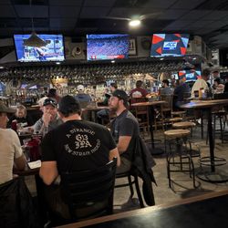 Trident Grills & Pizza Pub - Bar, table, patrons, tvs.