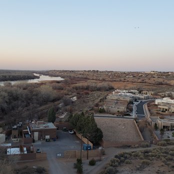 Fly Albuquerque - Fly Albuquerque  flyalbuquerque.com - A hot air balloon is seen floating in the sky above a desert landscape with a river and a residential neighborhood. - Hot Air Balloons Near Me - Albuquerque, New Mexico