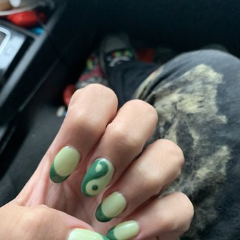 Lincoln Square Nails - Acrylic gel nails - A person's hand displays manicured nails with a yin-yang design in green and yellow, with a background of a car interior. - Nail Salons Near Me - Chicago, Illinois