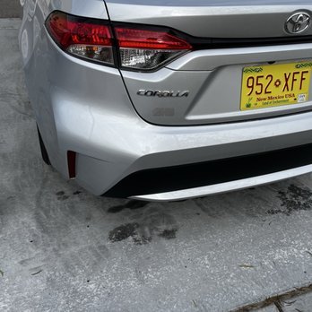 Caliber Collision - Repaired bumper - The photo captures the rear end of a silver Toyota Corolla parked on a concrete surface. The vehicle's taillights, model badge, and license plate from New Mexico are visible. The license plate reads '952 XFF' and includes the state name and slogan. The concrete surface has some dark stains and small debris, with a visible curb at the bottom of the image. - Body Shops Near Me - Rio Rancho, New Mexico