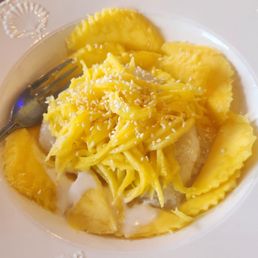Mango Sticky Rice - A white plate contains pineapple chunks and pasta topped with grated cheese, with a fork on the side. In the background, there are two small containers of dipping sauces.