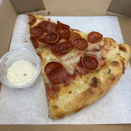 Pepperoni slice with parmesan cheese on the side