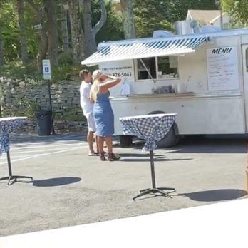 Roadside Bistro - two people ordering food from a food truck - Two women are at a food truck with a menu, in an outdoor parking lot with tables covered in checkered cloths. - Food Trucks Near Me - Newfoundland, Pennsylvania