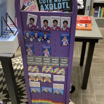 Words - Magnets - The purple book cart contains multiple rows of books and cards focused on LGBTQ+ topics, such as 'The Future is Female,' 'SAY GAY,' and 'Black Lives Matter.' The display is situated in a bookstore with shelves of books visible in the background, and the cart is positioned on a tiled floor. The arrangement includes illustrated cards and books promoting gender identity, equality, and pride. - Bookstores Near Me - Saint Paul, Minnesota