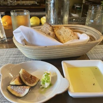 Primo - Bread Service and Amuse Bouche - A basket of bread with slices of toasted bread, a small dish of olive oil, and figs on a plate are arranged on a table at a restaurant. - Mediterranean Near Me - Rockland, Maine