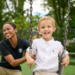 Primrose School at The Parks DC - Primrose Schools teacher pushing laughing boy on swing at outdoor childcare playground