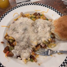 The Original Scrambowl - A breakfast plate featuring scrambled eggs, melted cheese, diced vegetables, and sausage, accompanied by a bread roll, on a checkered-rim plate.
