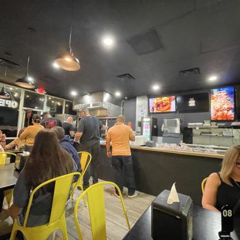 Between Two Buns - The restaurant filling up by the time we left there was a line going out the door - A restaurant interior with customers seated at tables, staff working behind the counter, and digital screens displaying food images. - Burgers Near Me - Miami, Florida