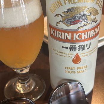 Pho Yummy - A glass of beer with a frothy head and a can of Kirin Ichiban beer are placed on a wooden table, with sunglasses in the foreground. - Vietnamese Near Me - Stuart, Florida