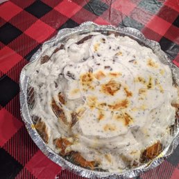 Chicken and Lamb Salad Mix - A dessert in a round, clear plastic container with a decorative edge, topped with whipped cream and caramel sauce. The container is placed on a red and black checkered tablecloth, and part of a fried food item is visible in the top left corner of the image.
