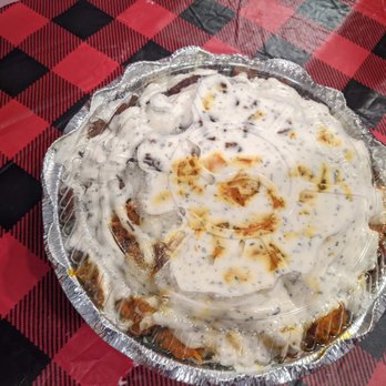 Halal Gyro Master - Chicken and Lamb Salad Mix - A dessert in a round, clear plastic container with a decorative edge, topped with whipped cream and caramel sauce. The container is placed on a red and black checkered tablecloth, and part of a fried food item is visible in the top left corner of the image. - Halal Near Me - River Vale, New Jersey
