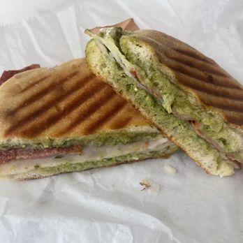 Java Hutt - Pesto Turkey Panini - A grilled panini sandwich featuring turkey, cheese, and pesto, with visible grill marks on the bread, placed on white paper. - Coffee & Tea Near Me - Hazel Park, Michigan