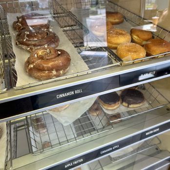 King Donuts - A glass display case shows cinnamon rolls, donuts, and other baked items, with labels like 'Cinnamon Roll' and 'Plain Jelly.' The case is part of a bakery or cafe setting. - Donuts Near Me - Newington, Connecticut