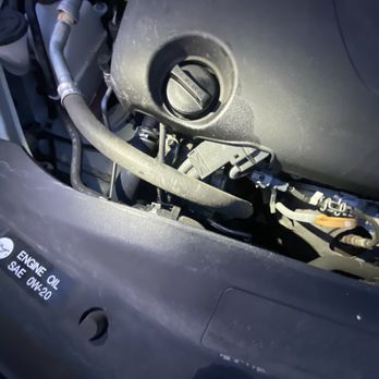 Firestone Complete Auto Care - Oil cap after 2nd time in the shop. Same exact spill, but not cleaned up - The image shows an open engine oil cap on a vehicle's engine, revealing engine parts and hoses, with a label indicating engine oil specifications. - Tires Near Me - Plainfield, Illinois